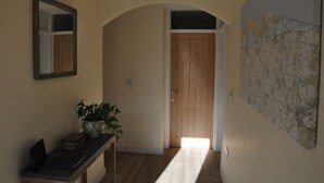 A hallway with a wooden door, a map on the wall, a potted plant, and a mirror. - Close-by is a spacious pet friendly bungalow close to the Quay - a hidden gem (Blakeney)
