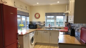 A compact kitchen with a red refrigerator, a microwave, a washing machine, and a sink. - Close-by is a spacious pet friendly bungalow close to the Quay - a hidden gem (Blakeney)