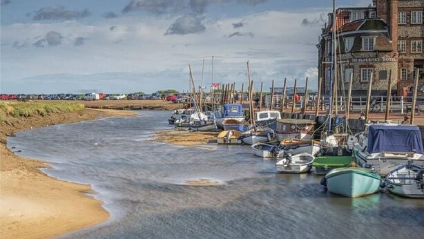 A riverside marina with boats docked, a sandy beach, and a historic building labeled "The Flannerby Hotel" in the background. - Close-by is a spacious pet friendly bungalow close to the Quay - a hidden gem (Blakeney)
