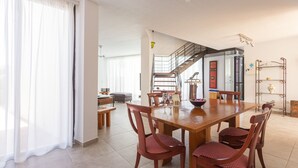 A spacious dining area with a wooden table and chairs, a staircase leading to an upper floor, and a kitchen in the background.