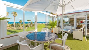 A covered outdoor seating area with a view of the ocean and a golf course.