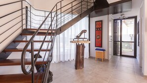 A modern staircase with metal railings and wooden steps, leading to a room with a wooden table and a chair.