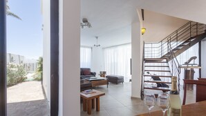 A spacious living area with a dining table, two wine glasses, and a bottle of wine. A staircase leads to an upper level, and a balcony is visible outside.
