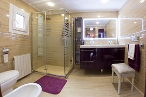 Une salle de bain moderne avec une douche à parois de verre, un meuble-lavabo avec miroir, une baignoire et un petit banc.