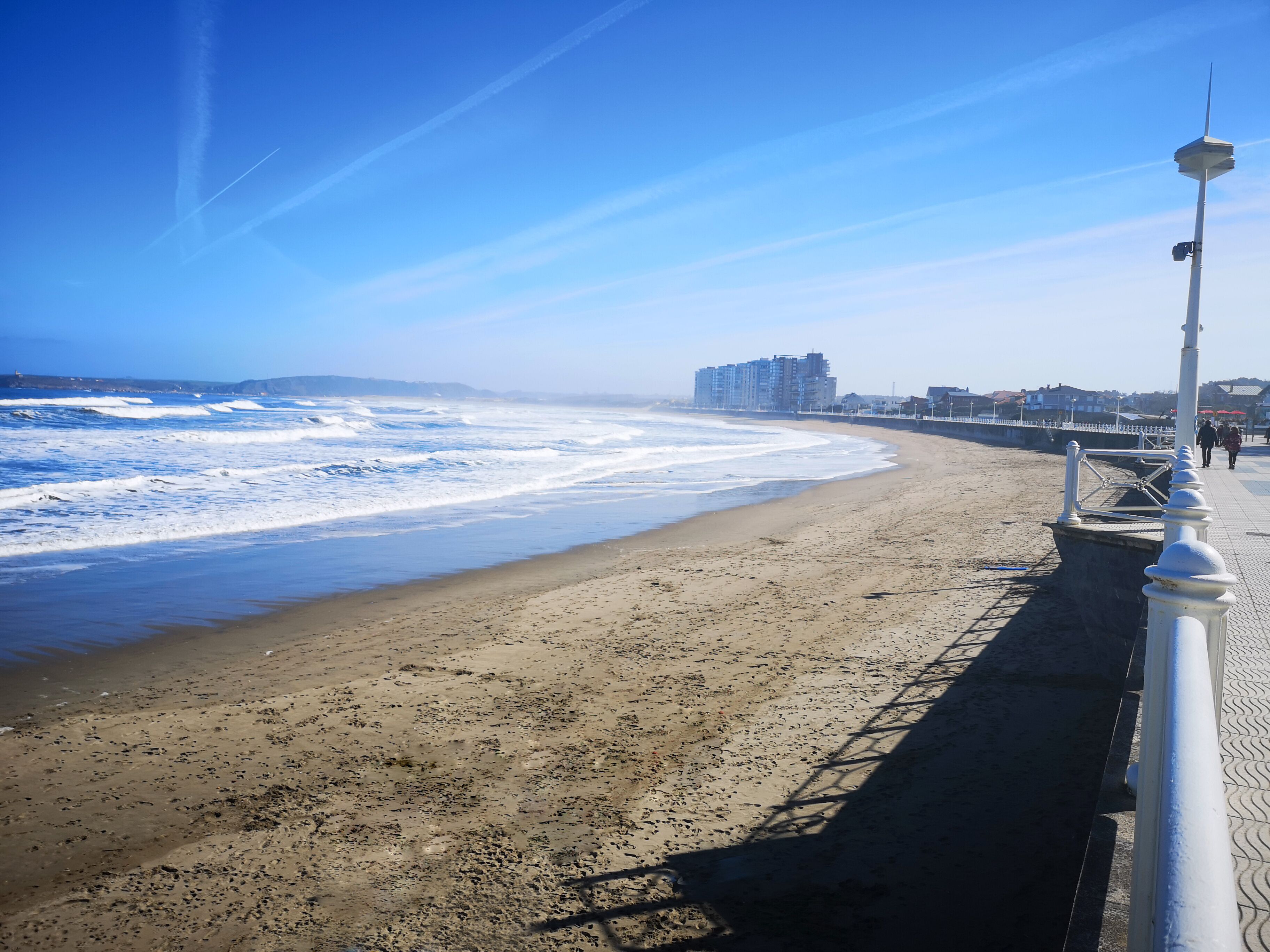 A beach with a promenade, ocean waves, and buildings in the background.