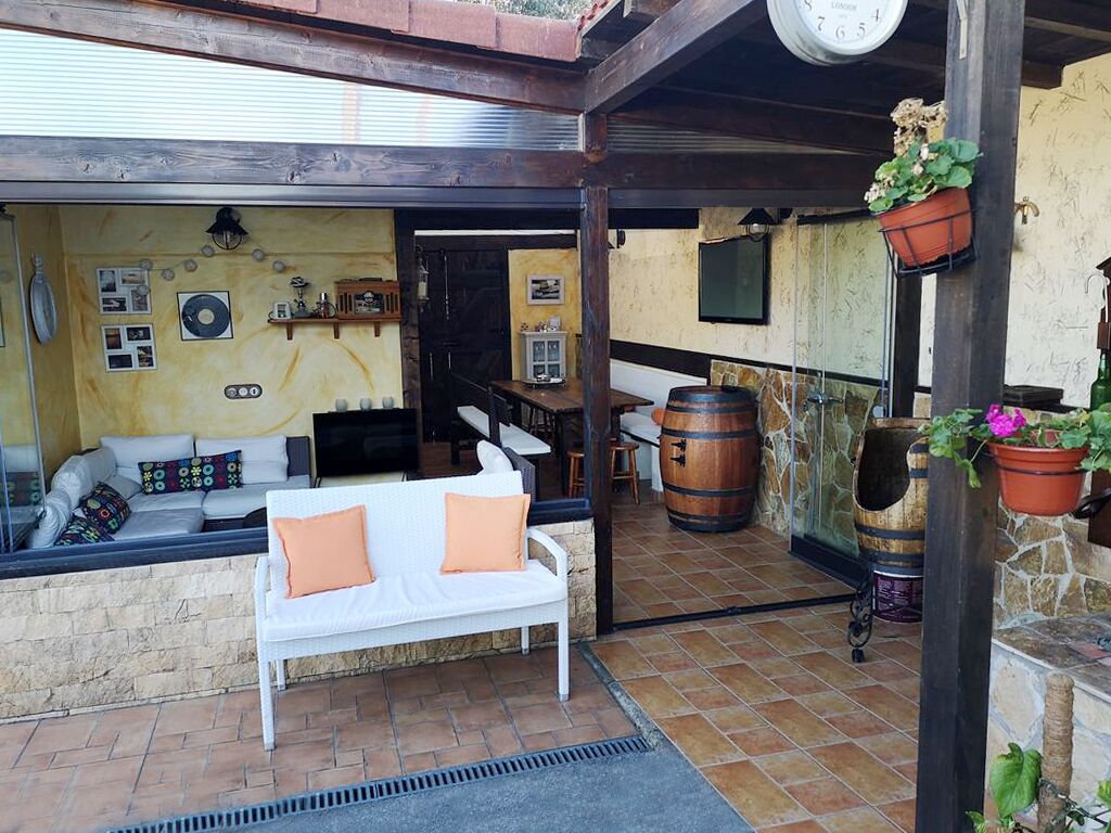 A cozy outdoor seating area with a white sofa, a wooden table, and a barrel.