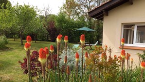 Ein Garten mit hohen Pflanzen und einer Terrasse mit Tisch und Stühlen.
