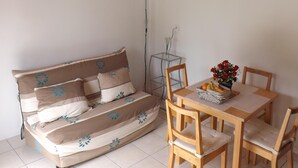 Ein gemütliches Zimmer mit Holzbalkendecke, einer Couch mit gemusterten Kissen, einem Esstisch mit Stühlen und einem kleinen Glastisch mit Vase und Obstschale.