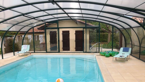 Ein überdachter Pool mit Liegestühlen und einer Tür zu einer überdachten Terrassenfläche.