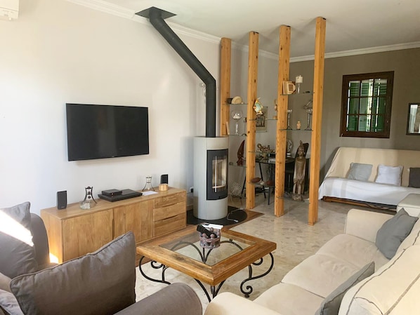 A living room with a fireplace, sofa, TV, and wooden beams.