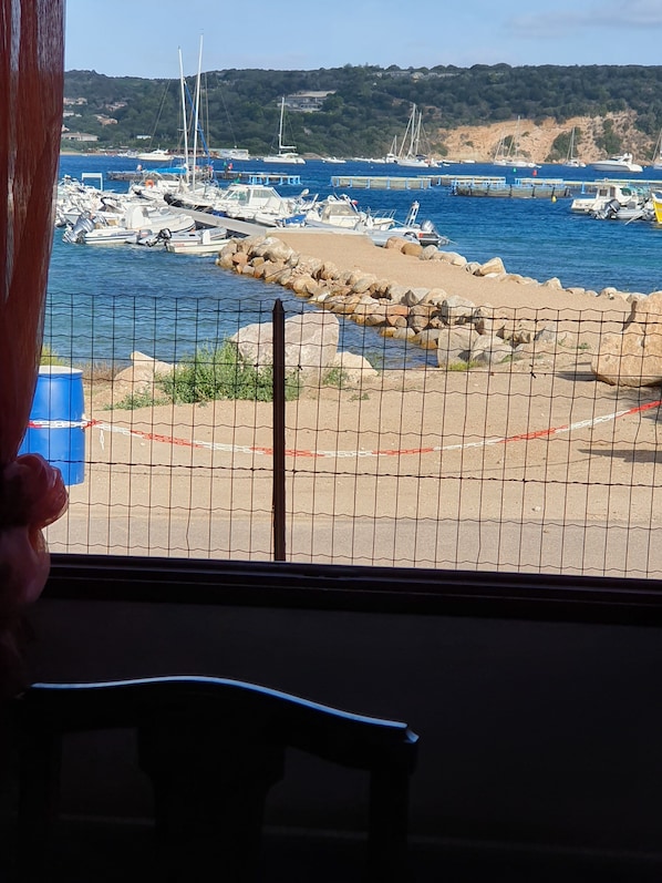 A view of a marina with boats docked, a rocky shoreline, and a fence in the foreground.