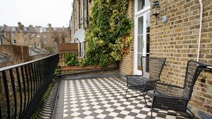 Un balcon avec un sol à carreaux, deux fauteuils en osier, un mur en briques et une fenêtre.