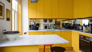Une cuisine avec des meubles de couleur jaune, un plan de travail en marbre, un évier et une cuisinière.