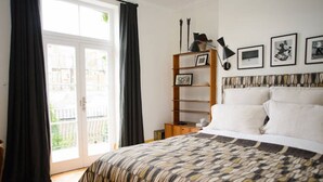 Une chambre à coucher comprenant un lit, une table de chevet, une étagère avec des photos encadrées et une fenêtre avec des rideaux.