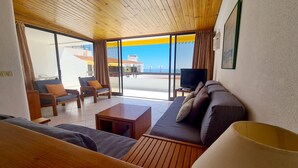 A living room with a wooden ceiling, a sofa, a coffee table, and a TV. There are two chairs and a window with curtains. - Albufeira, Sea Balcony (11) (Albufeira)