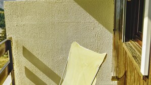 Un balcón con un muro texturizado, una silla plegable y barandilla de madera.
