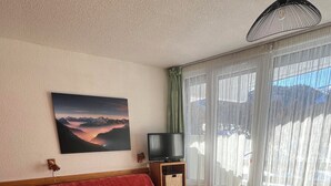 Un salón acogedor con un sofá rojo, una mesa de centro de madera y un televisor sobre un mueble.