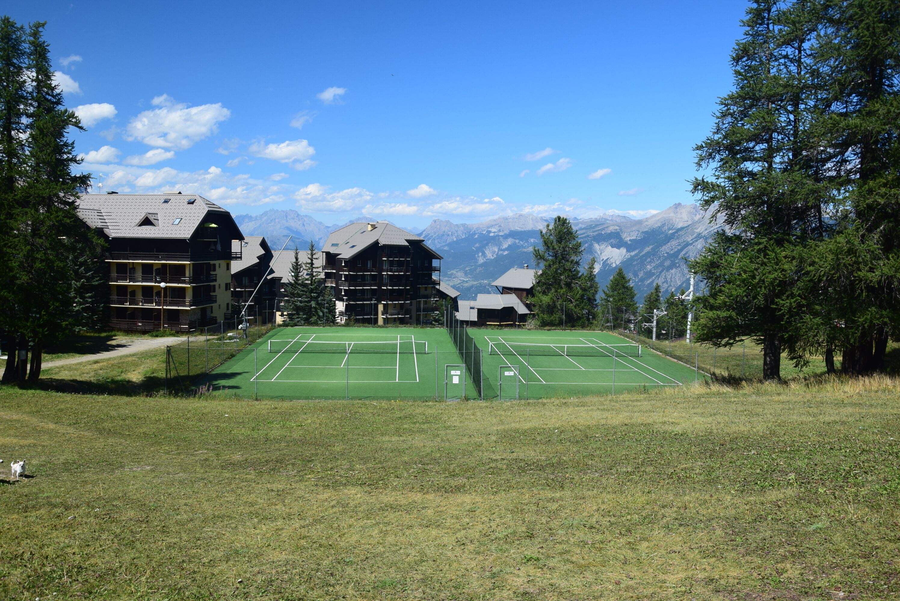 A tennis court surrounded by buildings with a mountain view.