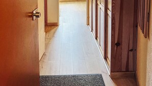 Un pasillo con puertas de madera, un felpudo y un suelo de tonos claros.