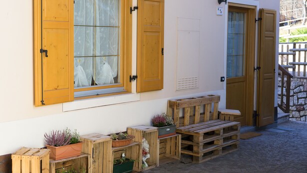 Un bâtiment avec des volets en bois, un banc et des plantes en pot.