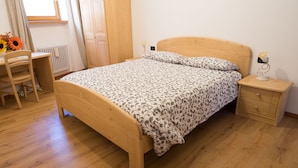 Un lit en bois avec une couvre-lit à motifs, une table de chevet en bois avec une lampe, une chaise en bois et un radiateur.