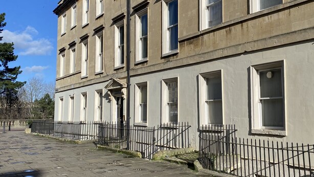Une rangée d’immeubles uniformes, à plusieurs étages, présentant un style architectural cohérent, avec des fenêtres régulièrement espacées et une façade symétrique.