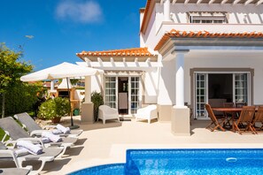 A poolside area with lounge chairs, a dining table, and a covered patio.