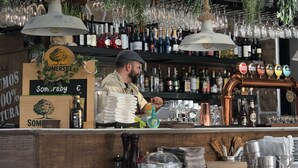 Un'area bar con scaffali pieni di bottiglie, bicchieri appesi al soffitto e un bancone con una pila di piatti e una bottiglia d'acqua.