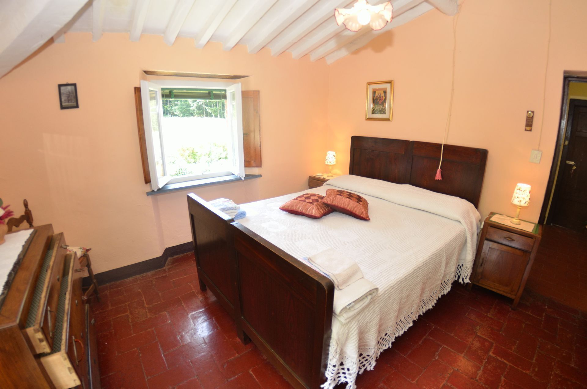 Une chambre avec un lit en bois, une fenêtre donnant sur un beau paysage, une table de chevet avec une lampe et une porte.