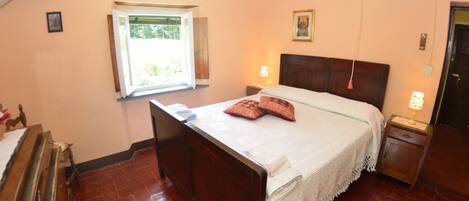 Une chambre avec un lit en bois, une fenêtre donnant sur un beau paysage, une table de chevet avec une lampe et une porte.