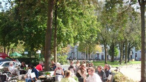 A group of people sitting at tables outdoors, surrounded by trees and greenery.
