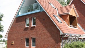 A red brick house with a sloped roof, large windows, and a visible balcony.