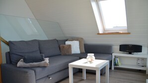 A modern living room with a grey sofa, a white coffee table, and a TV on a white stand.