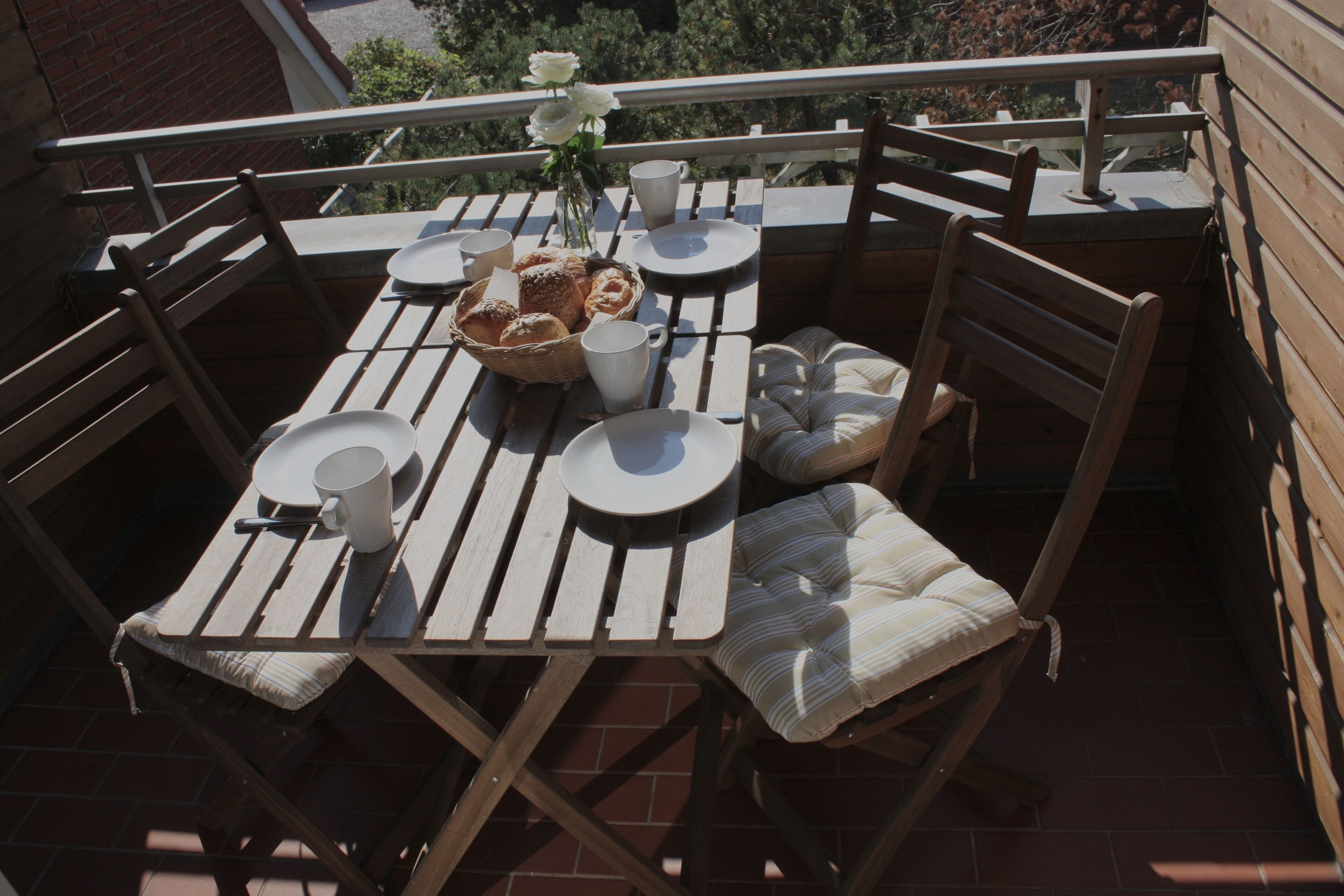 A wooden outdoor dining set with chairs, a table, and a basket of bread.
