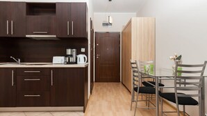 Une cuisine compacte avec des meubles en bois foncé, une hotte de cuisine en acier inoxydable et un petit coin repas avec des chaises en métal et une table en verre.