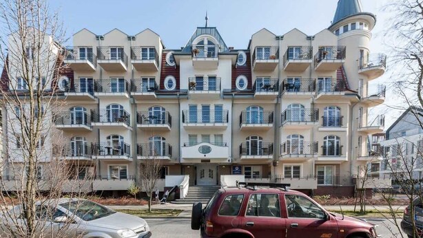 Un immeuble résidentiel à plusieurs étages, doté de balcons, d’une entrée centrale et d’une structure distinctive en forme de tourelle.