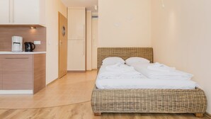 Een slaapkamer met een rieten bed, een nachtkastje en een kleine kitchenette met een koffiezetapparaat.