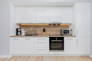 Una cocina moderna con gabinetes blancos, horno empotrado, microondas y cafetera.