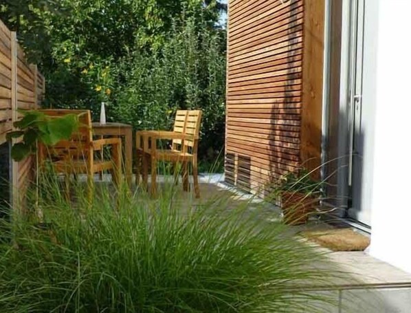 Une terrasse en bois avec deux chaises et une table en bois, entourée d’un luxuriant feuillage verdoyant.
