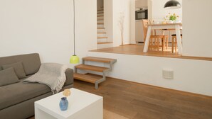 Moderni olohuone, jossa on sohva, sohvapöytä ja portaat, jotka johtavat keittiötilaan.