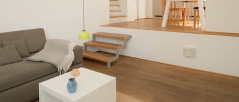 A modern living room with a sofa, coffee table, and a staircase leading to a kitchen area.
