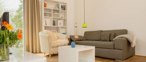 A modern living room with a white coffee table, a grey sofa, a white bookshelf, and a vase with flowers.