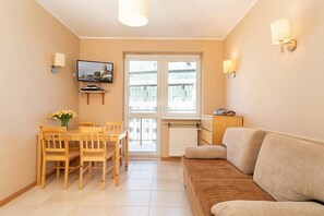 Une pièce comprenant une table à manger, des chaises, un canapé, un téléviseur et une fenêtre avec des stores.
