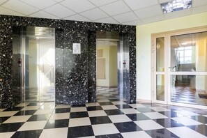 Un vestíbulo con piso a cuadros, paredes de mármol y puertas de cristal que dan a los ascensores.