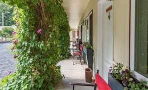 A covered outdoor seating area with chairs and tables, surrounded by lush greenery and flowering plants.