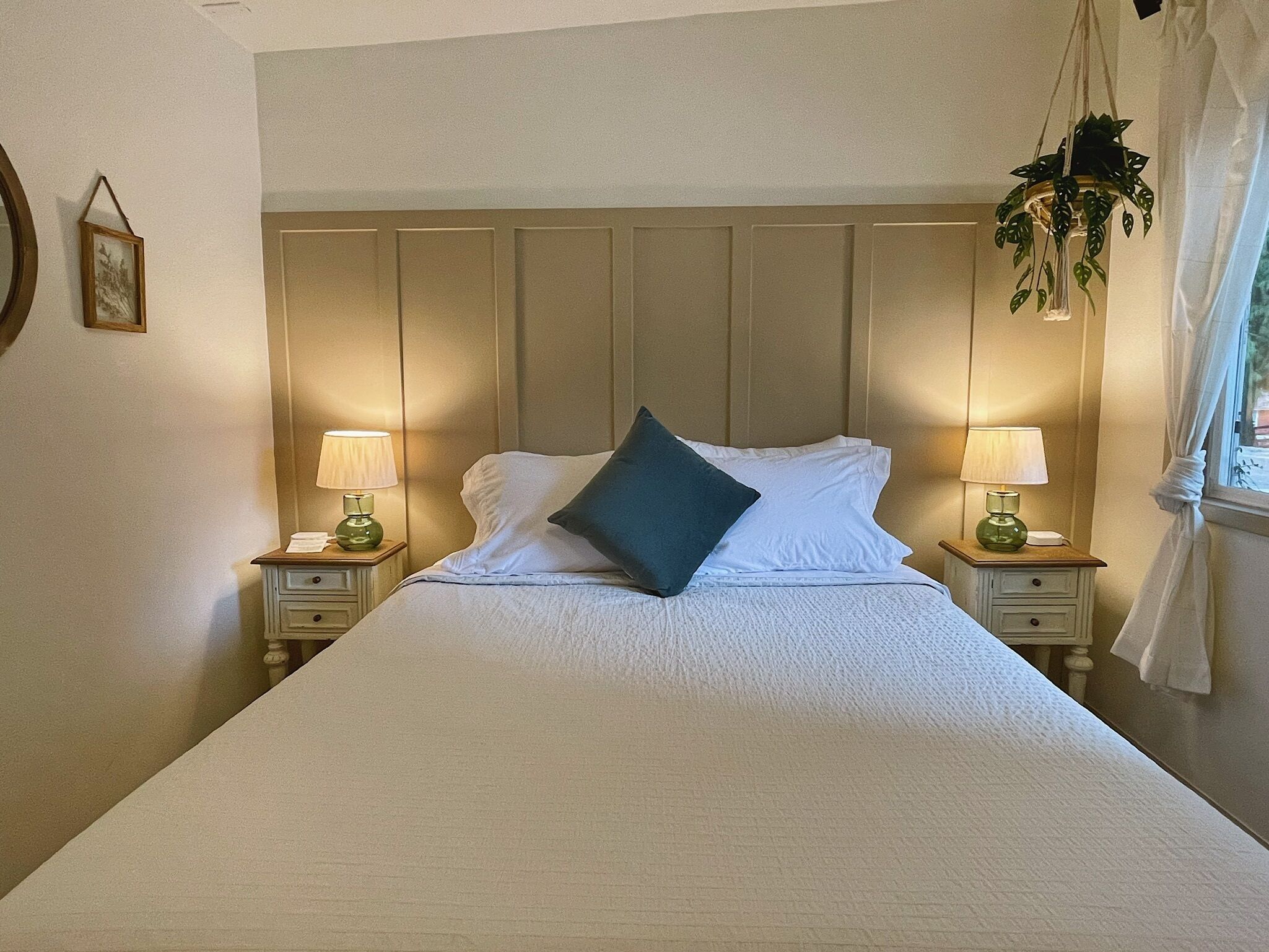 Una cama bien tendida con sábanas blancas y un almohadón azul oscuro, flanqueada por dos mesitas de noche con lámparas.