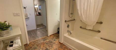 A bathroom with a bathtub, shower, and a sink area.