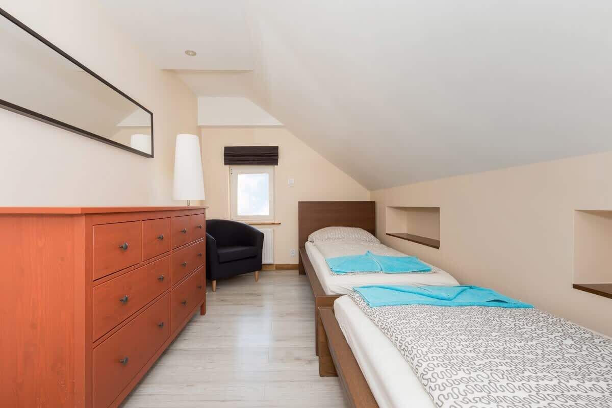 A small, well-lit room with two beds, a dresser, a chair, and a window.