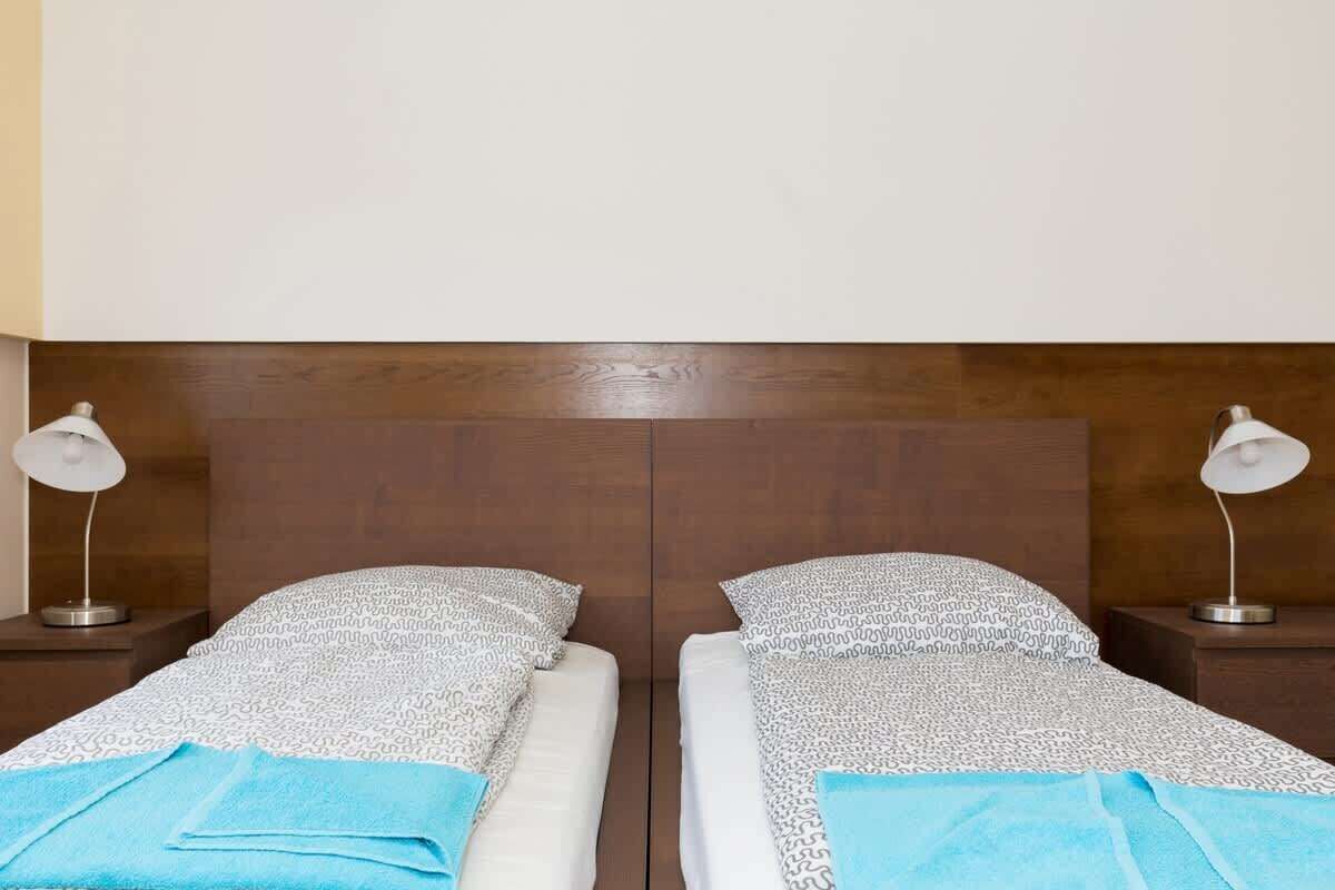 Een hotelkamer met twee enkele bedden, elk voorzien van een bedspread met dessin en een blauwe handdoek. Er staan twee bedlampen op houten nachtkastjes.