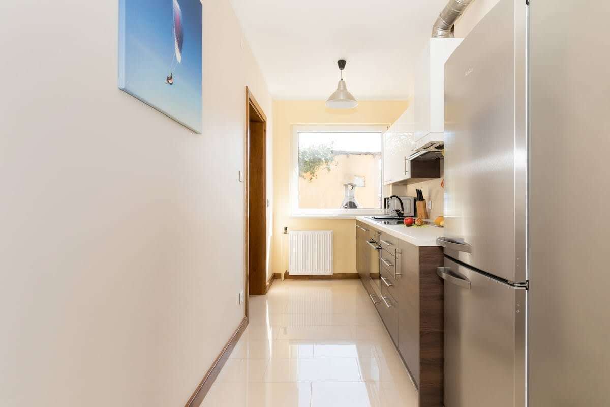A modern kitchen with a stainless steel refrigerator, a window providing natural light, and a white radiator.